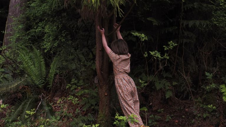 A child playing in the woods wearing a gender-neutral gingham playsuit from Red Creek Kids