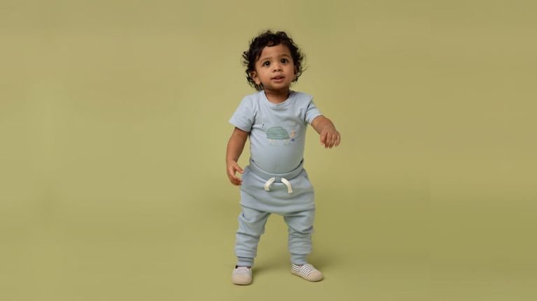 A child models gender-neutral sweatpants, shoes and a t-shirt from Rise Little Earthling
