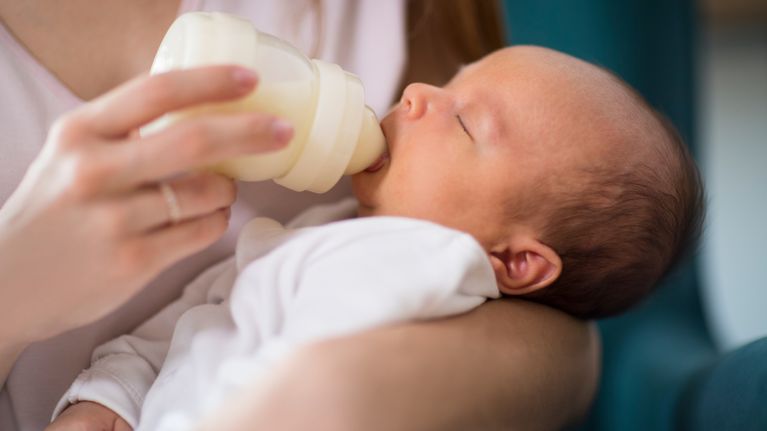 Close Up Of Loving Mother Feeding Newborn Baby Son With Bottle At Home