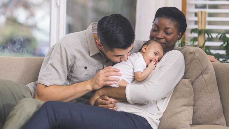 couple snuggle with their infant daughter on the couch in their living room