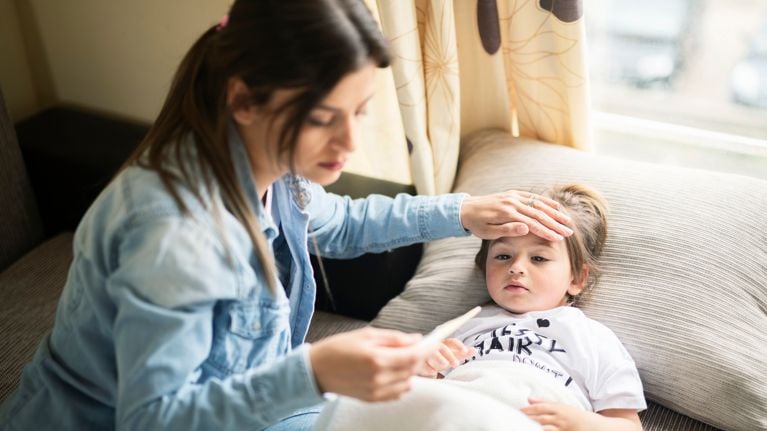 Mother checking temperature on sick daughter laying in bed