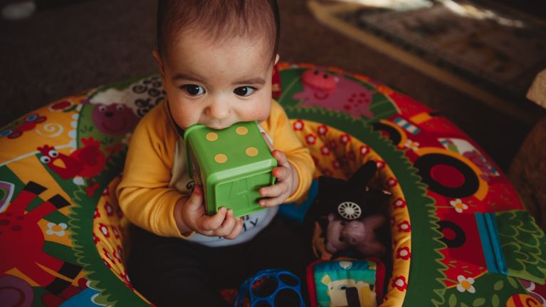 6 Month Old Baby Boy Sits in Living Room in an Infant Seat Playing with Blocks