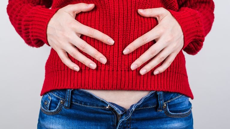  Cropped close up photo of unhappy sad upset girl eating unhealthy lot of sweets dessert holding hands on red pullover feeling ill isolated grey background