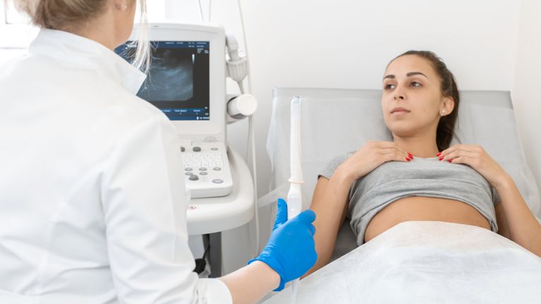 A gynecologist sets up an ultrasound machine to diagnose a patient who is lying on a couch. A transvaginal ultrasound scanner of the internal organs of the pelvis.