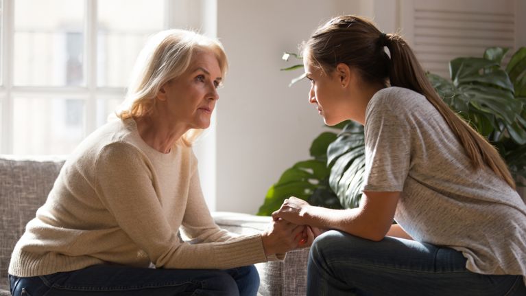 Grown up daughter holding hands of middle aged mother relatives female sitting look at each other having heart-to-heart talk, 