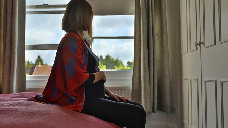 Lone pregnant woman sitting on the bed looking out at the window in the morning