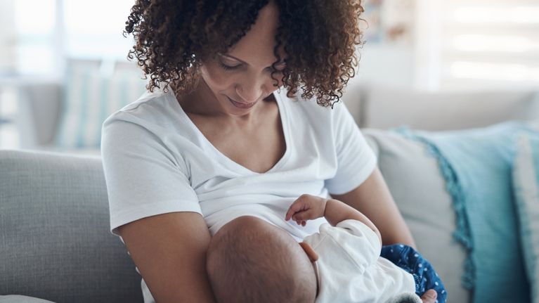 Shot of a young woman breastfeeding her adorable baby girl on the sofa at home