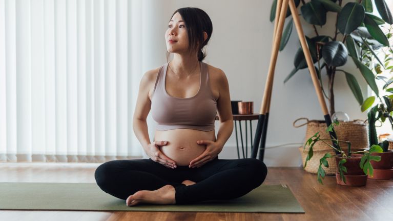 Beautiful young pregnant woman resting after doing pregnancy yoga at home. Healthy and active pregnancy lifestyle concept.