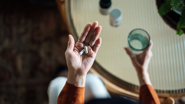 Overhead view of senior Asian woman feeling sick, taking medicines in hand with a glass of water at home. 