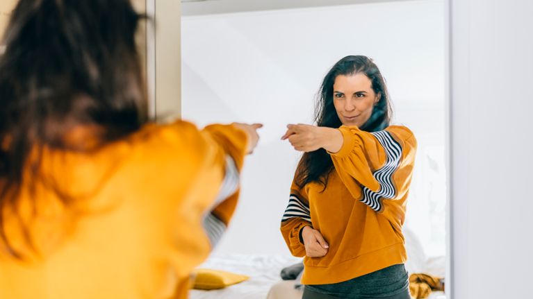 Self confident single woman pointing finger at her reflection in mirror, dancing and felling good