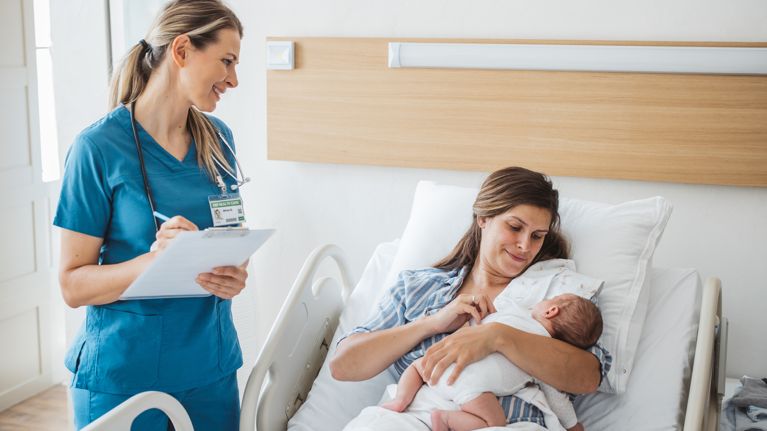 Nurse taking personal data from mother and talking to her. Mother holding newborn baby.