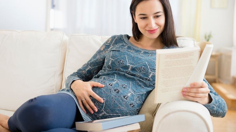 Pregnant woman reading baby books on sofa