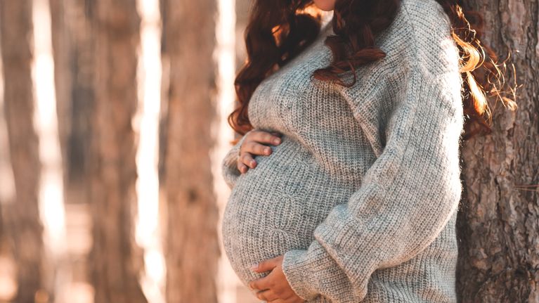 Pregnant woman 30-35 year old wearing warm knitted sweater posing outdoors.