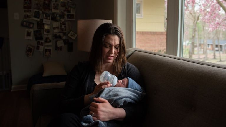 photo of woman bottle feeding a new baby