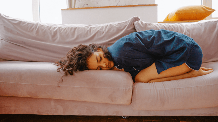 woman curled up on the couch looking in pain