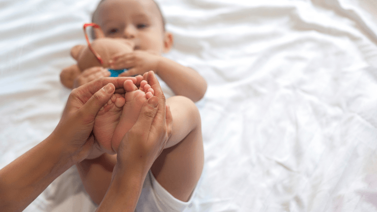 baby lying on a bed with someone holding its feet