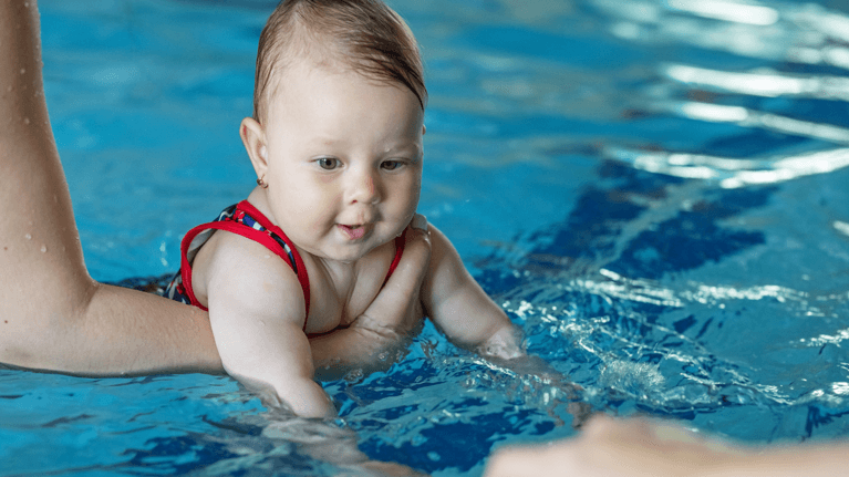 baby swimming in a pool while a parent holds on to her