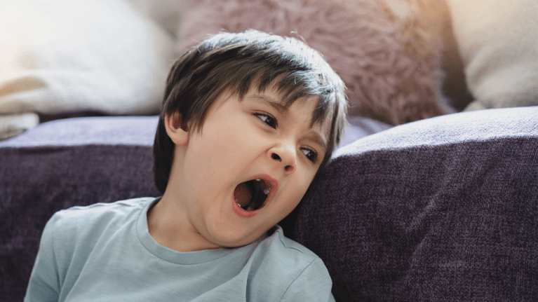 young boy leaning against a couch cushion yawning