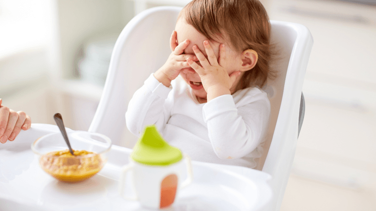 baby eating from bowl of pureed corn sitting in a high chair