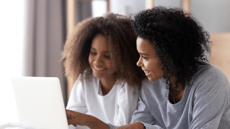 mom and daughter sitting at a kitchen table looking at a laptop together