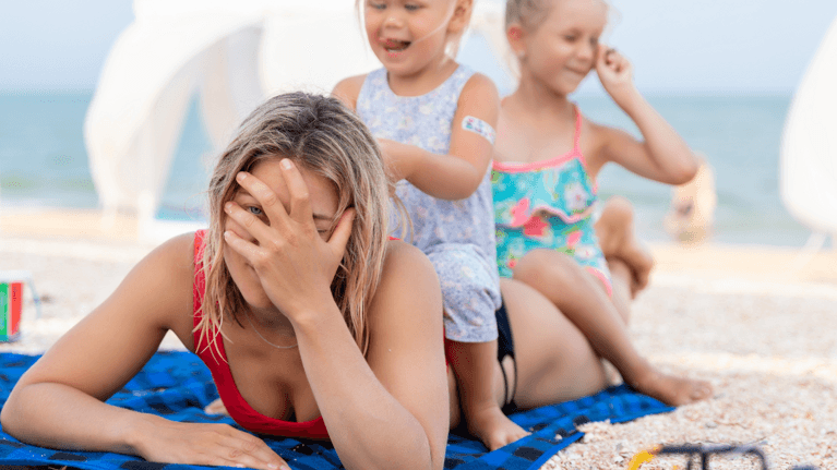 mom laying on the beach with kids sitting on top of her