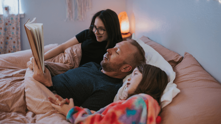 dad reading a story to his daughters in bed