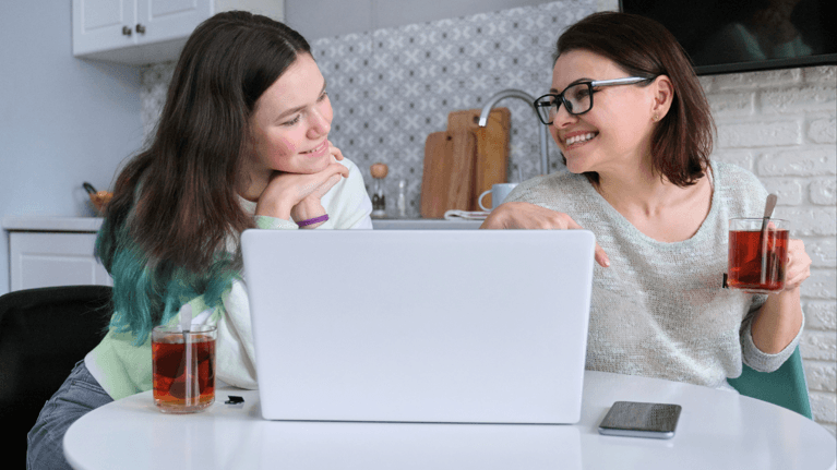 mom and daughter sitting at a kitchen table looking at a laptop together