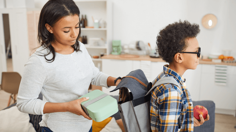 mom putting a lunch box in her son's backpack