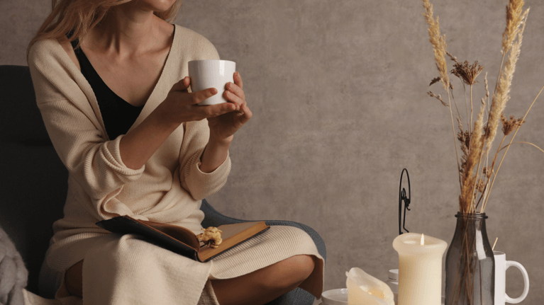 woman sitting holding a mug next to a table with candles on it