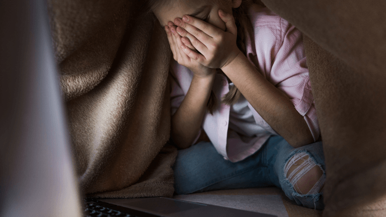 little girl looking at a computer screen crying with her head in her hands