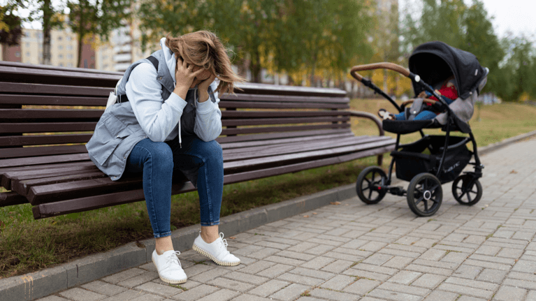 woman sitting on a park bench looking upset with a baby stroller next to her