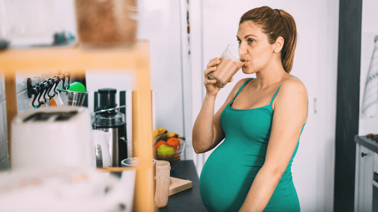 pregnant woman standing next to a smoothie bar drinking a shake