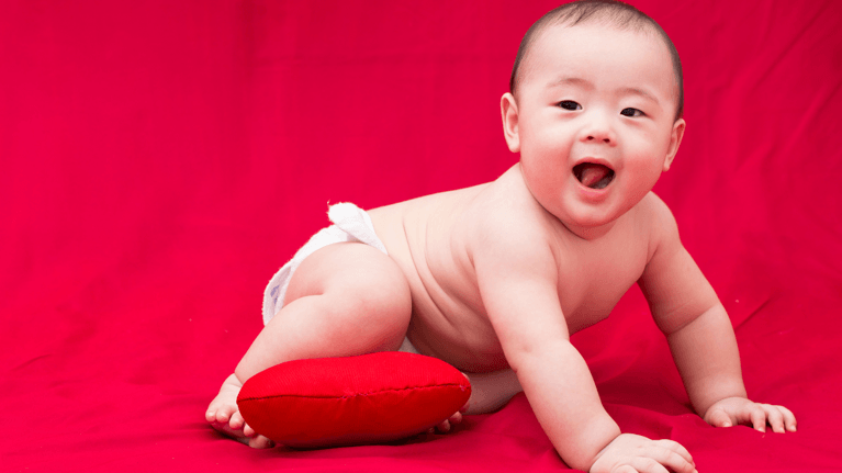 young baby crawling on a red background holding with a stuffed red heart