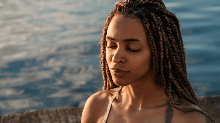 woman with eyes closed meditating near the water