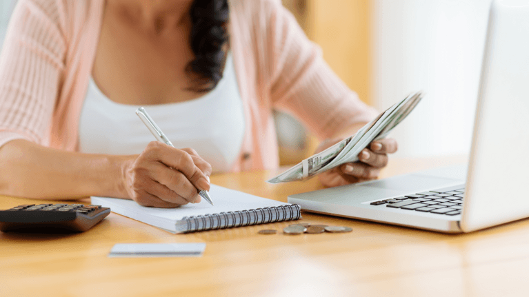 woman sitting at a table with a computer and holding money