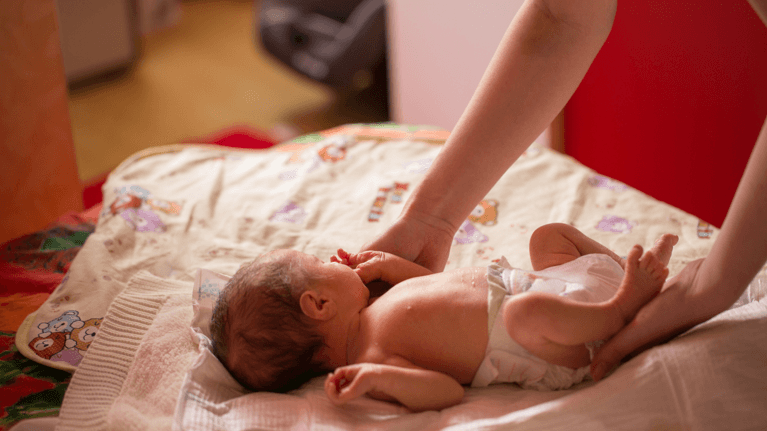 baby lying on a bed with someone reaching over to comfort him