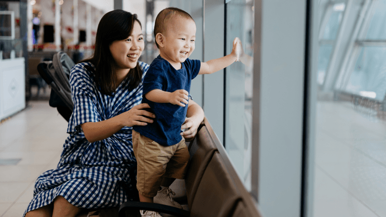 Young Asian mom sitting with her baby boy at the airport looking out the window